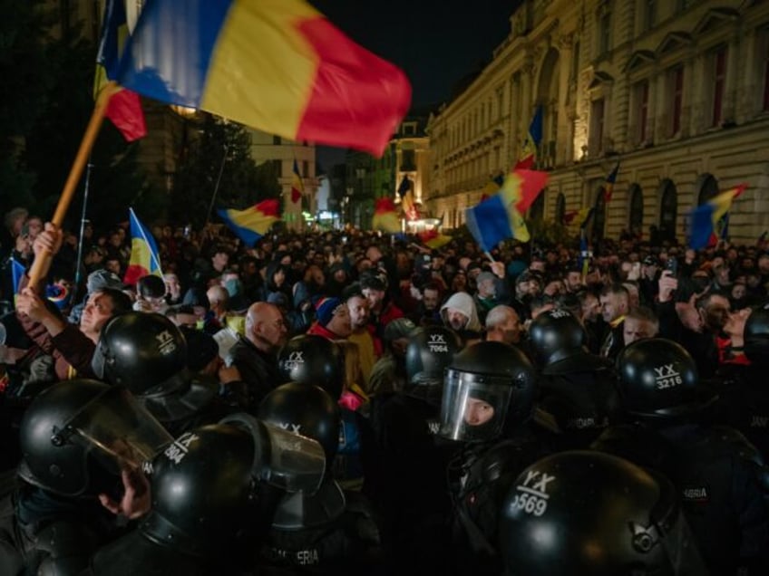 Romanian gendarmes in riot gear walk past a fire as they face protesters amid clashes duri