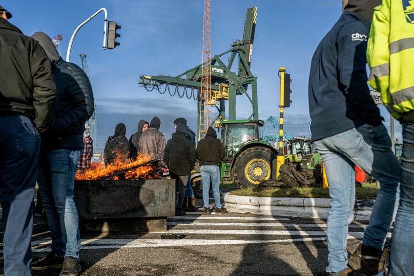 Farmers stand beside tractors and a fire, during a protest organized by several agricultural unions at quai 730 near the port of Antwerp on February 13, 2024. Farmers are protesting across Europe as they demand better conditions to grow, produce and maintain a proper income. (Photo by JONAS ROOSENS / Belga / AFP) / Belgium OUT (Photo by JONAS ROOSENS/Belga/AFP via Getty Images)