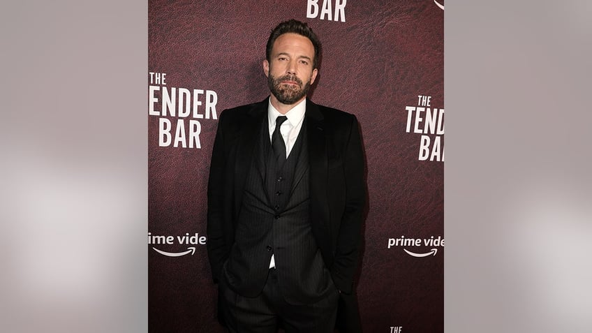 Ben Affleck in a three=-piece black suit and black tie looks serious on the carpet