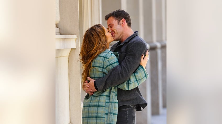 Jennifer Lopez in a green plaid jacket kisses a smiling Ben Affleck who wraps his arms around her