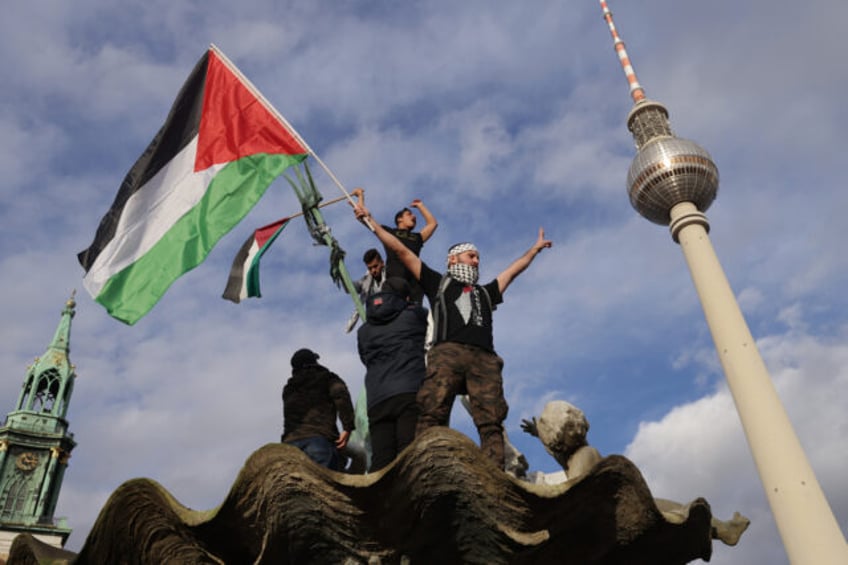 BERLIN, GERMANY - NOVEMBER 04: A man waves a Palestinian flag from atop Neptune Fountain d