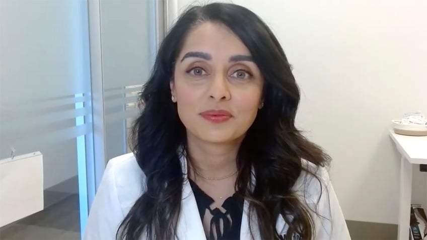 Dr. Priya Mistry, a woman with long black hair and wearing a doctor's coat, looking at the camera.