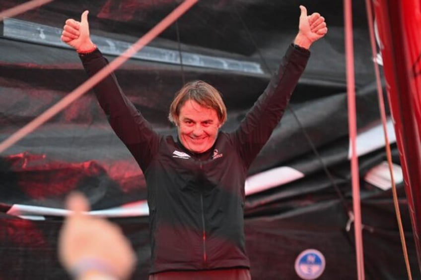 A red flare illuminates French skipper Yannick Bestaven as he waves from aboard his Imoca