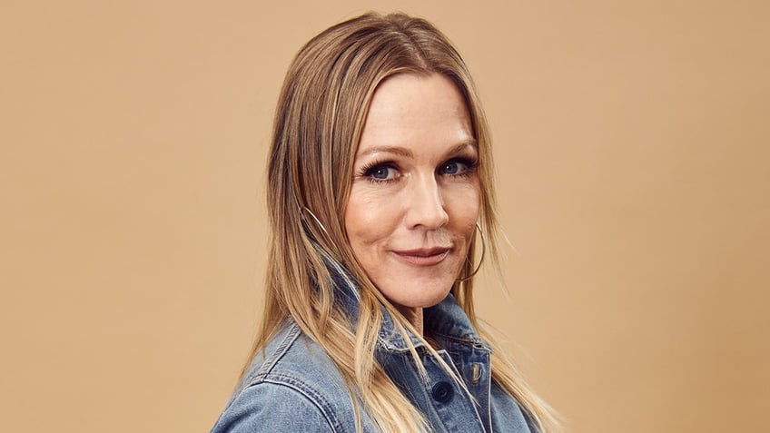 Jennie Garth in a denim jacket looks at the camera with her body angled