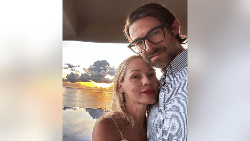 Jennie Garth soft smiles as she leans into husband Dave Abrams in a patterned shirt with a stunning sunset in the background