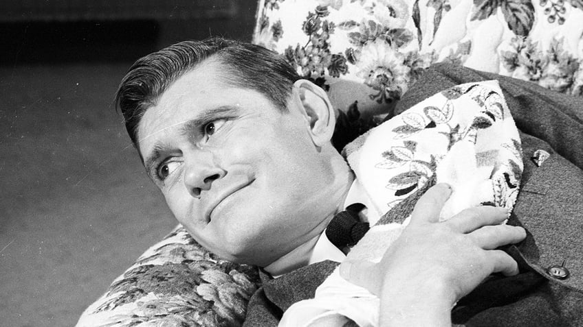 Dick York laying down on a floral couch and smiling.