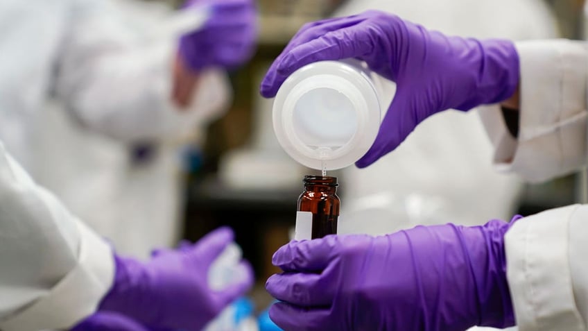 A water researcher, pours a water sample into a smaller glass container for experimentation as part of drinking water and PFAS research