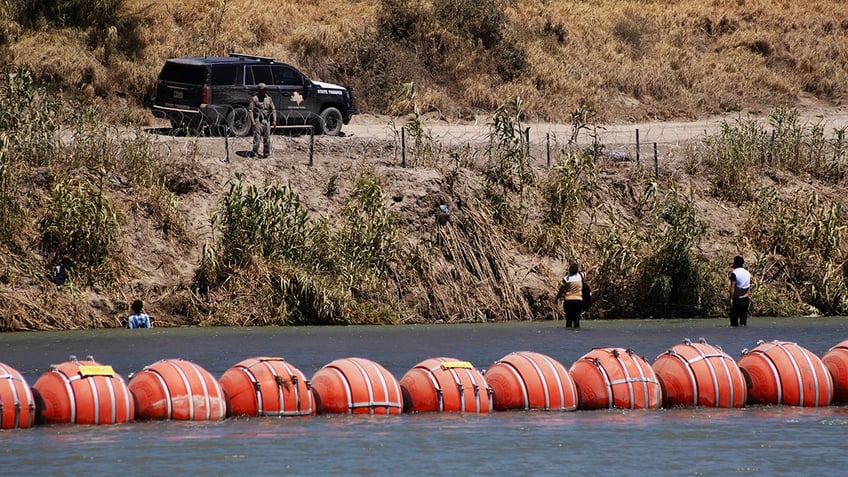 floating buoy barrier in middle of Rio Grande with border officer watching in background