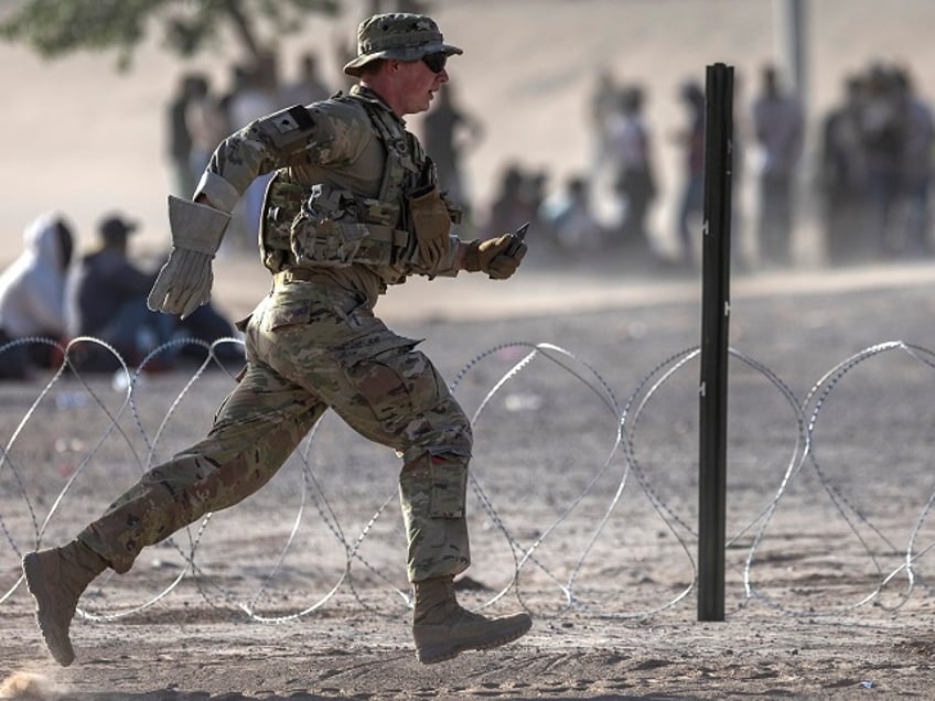 EL PASO, TEXAS - MAY 10: A Texas National Guard soldier runs while setting up razor wire around a makeshift immigrant camp located between the Rio Grande and the U.S.-Mexico border fence on May 10, 2023 in El Paso, Texas. The number of immigrants reaching the border has surged with the end of the U.S. government's Covid-era Title 42 policy, which for the past three years has allowed for the quick expulsion of irregular migrants entering the country. (Photo by John Moore/Getty Images)