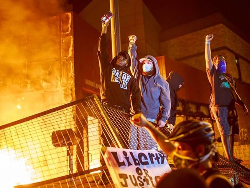 Protesters hold up their fists as flames rise behind them in front of the Third Police Pre