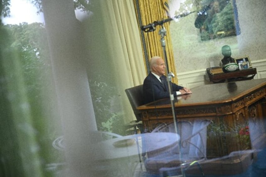 Seen through a window, US President Joe Biden speaks during an address to the nation from