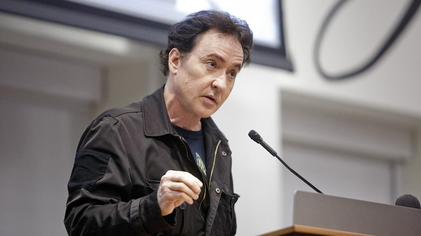 John Cusack standing at a podium