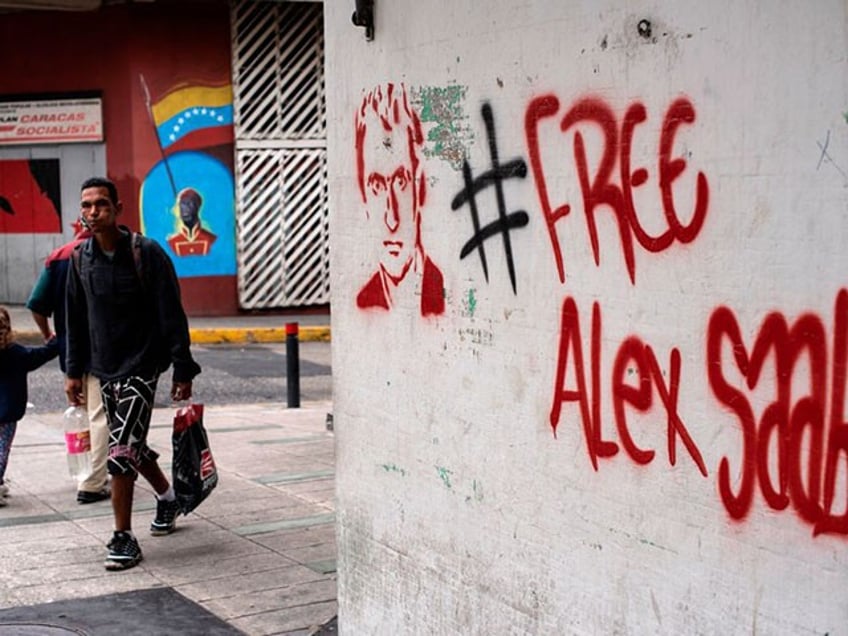 People walk near a graffiti demanding Colombian businessman Alex Saab's freedom, in Caracas, on February 23, 2021. - Saab, who is allegedly close to Venezuelan President Nicolas Maduro and wanted in the US for money laundering, has been put under house arrest in Cape Verde. Saab was detained in June 2020 as a plane he was travelling on stopped over in the African country. (Photo by Yuri CORTEZ / AFP) (Photo by YURI CORTEZ/AFP via Getty Images)