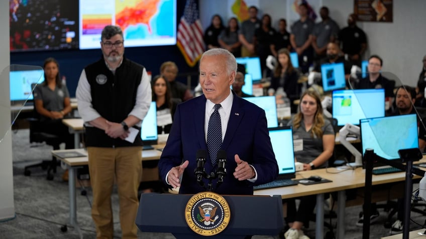 President Joe Biden stands at a podium in the D.C. Emergency Operations Center in front of a map of the country displaying heat data.