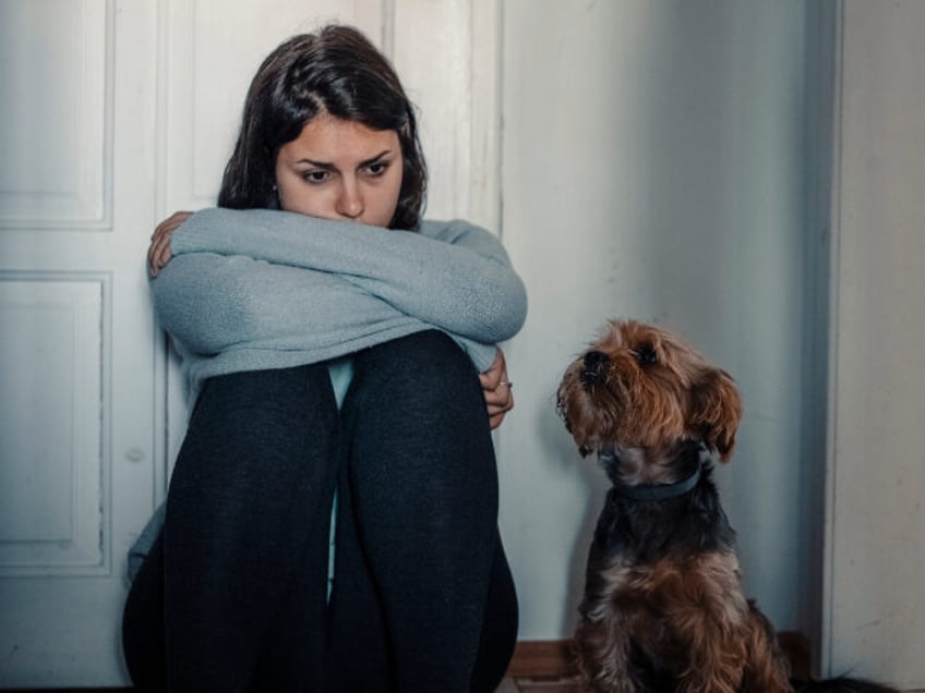 Woman With A Mental Problems Is Sitting Exhausted On The Floor With Her Dog Next To Her -