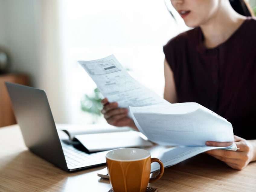 Cropped shot of Asian woman sitting at dining table, handling personal finance with laptop. She is making financial plan and planning budget as she go through her financial bills, tax and expenses at home. Wealth management, banking and finance concept