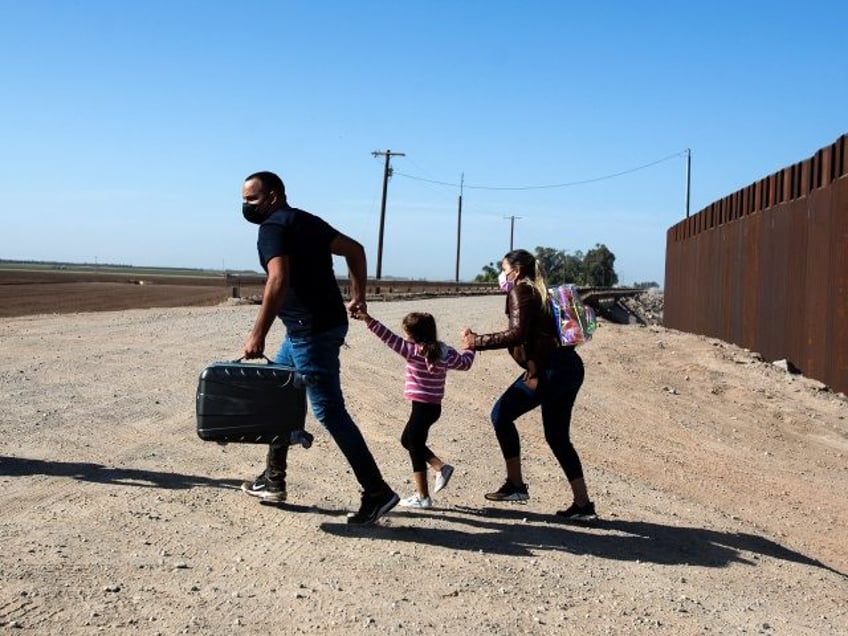 A family of migrants from Cuba runs across the border by the wall separating the United St