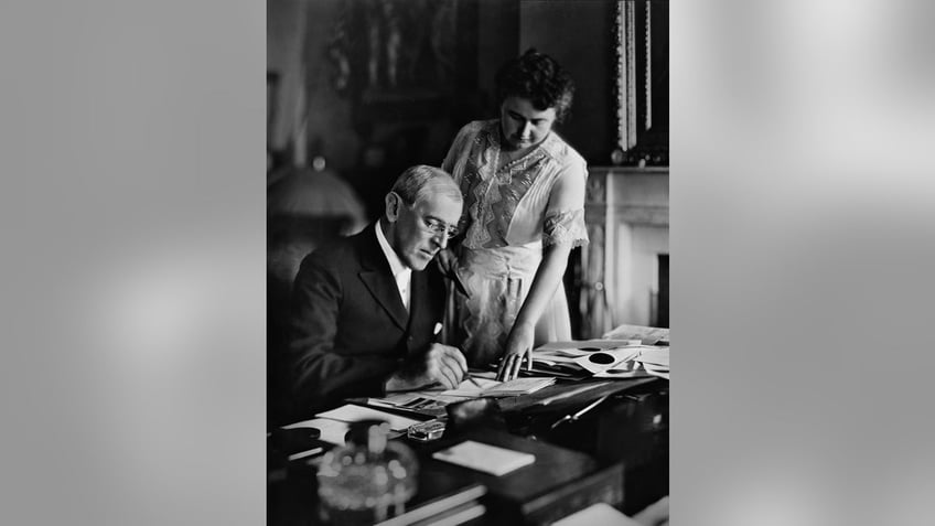 Woodrow Wilson (1856-1924), president of the United States from 1913-1921, goes over papers at his desk as his second wife Edith Bolling Galt Wilson looks on, mid 1910s. Edith was often referred to as "secret president" because of the important role she played in Wilson's presidency during his long and debilitating illness following a stroke.