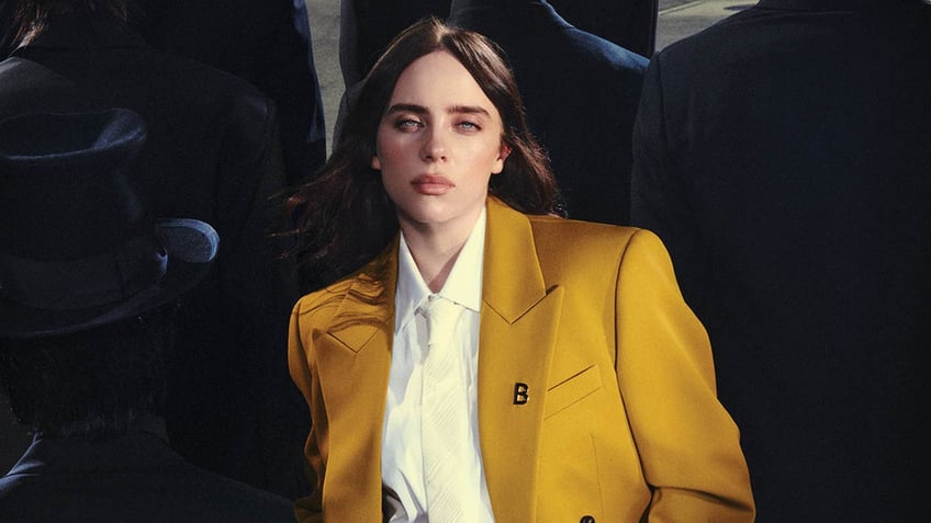 billie eilish in a yellow suit with shadows of men with top hats in the background