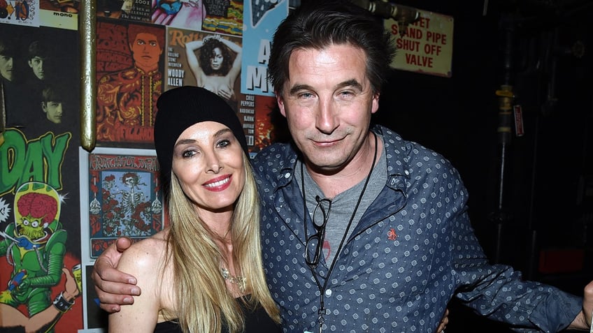 Chynna Phillips wearing a black beanie smiles next to husband Billy Baldwin in a blue patterned shirt