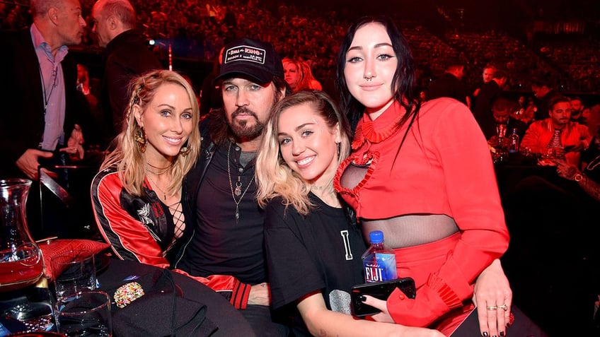 Tish Cyrus wraps her arm around Billy Ray Cyrus who sits next to Miley Cyrus with Noah Cyrus sitting on her lap