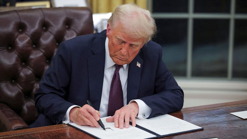 President Donald Trump signs documents in the Oval Office