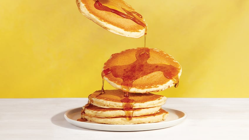 A pancake stack that has the top two pancakes falling on to the stack with syrup showing.