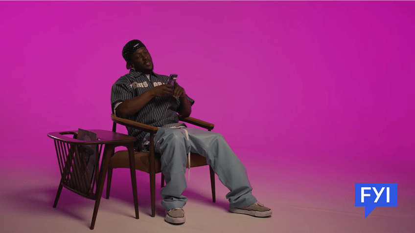 Hit Boy sitting in a chair with his phone speaking to AI app