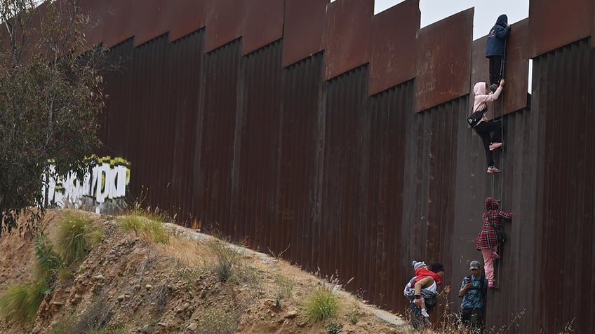 A group of adult and child migrants are smuggled across the Tijuana-San Diego border as they climb the wall to seek asylum to the United States in Tijuana, Baja California, Mexico, on June 7, 2024.