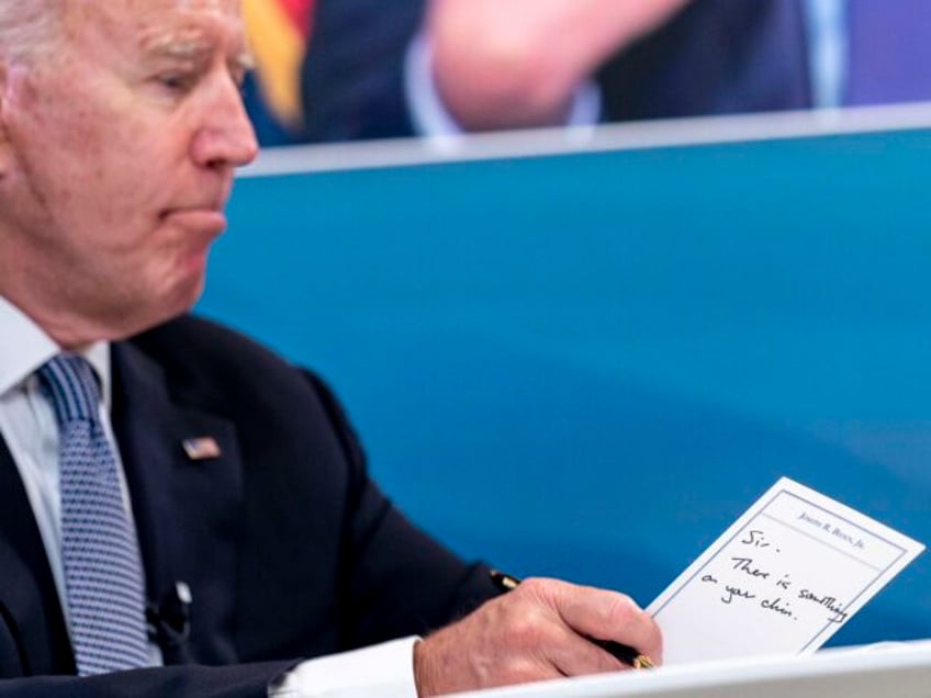 President Joe Biden holds a card handed to him by an aide that reads "Sir, there is s