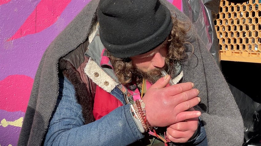 Man smokes out of glass pipe on sidewalk