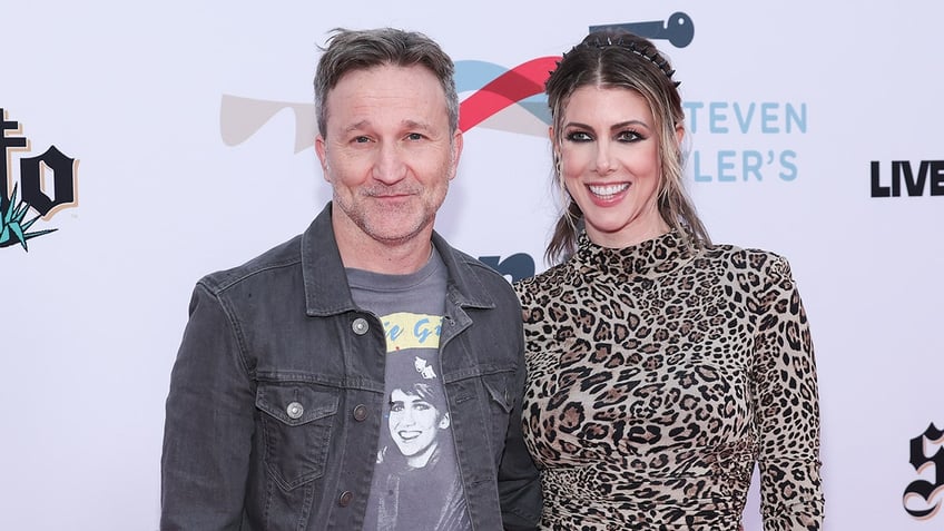 Breckin Meyer in a black jean jacket and t-shirt soft smiles on the carpet next to girlfriend Kelly Rizzo in a leopard print dress