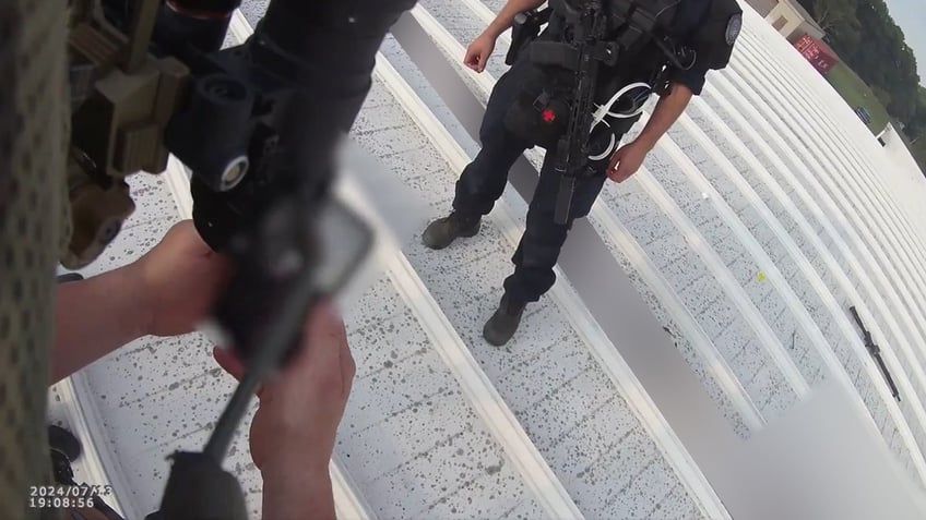 Two Beaver County Emergency Services officers stand on a roof. One shows a member of the U.S. Secret Service information on his cell phone after finding the body of Thomas Crooks.