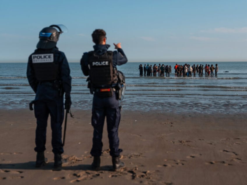 GRAVELINES, FRANCE - JUNE 17: Police officers look on as migrants wade in the sea to try a