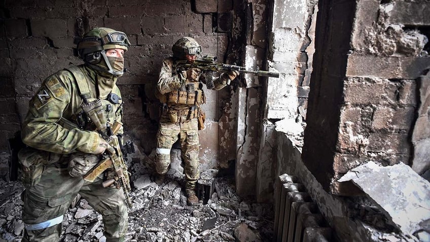 Two soldiers patrol wreckage with guns.