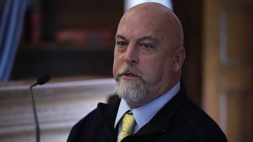 Brian Albert wears a blue shirt, yellow tie and dark jacket on the witness stand