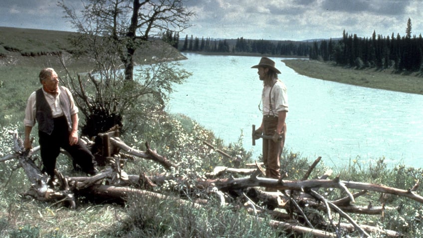 Sir Anthony Hopkins looks at Brad Pitt during a scene outside for "Legends of the Fall" by water and surrounded by wood