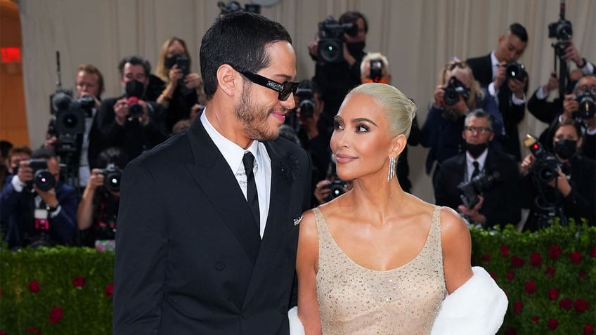 Kim Kardashian in a gold sparkly Marilyn Monroe dress looks up at Pete Davidson wearing sunglasses on the Met Gala red carpet