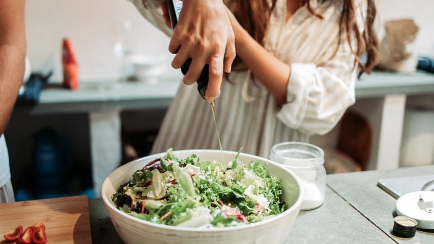 woman dresses salad with oil