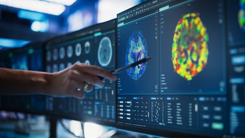 Doctor Pointing At Desktop Computer Monitor With CT Scan Of Patient's brain