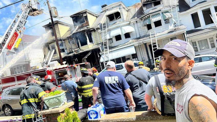 Fire rescue hero stands in the street as firefighters hose down the burnt-out house.