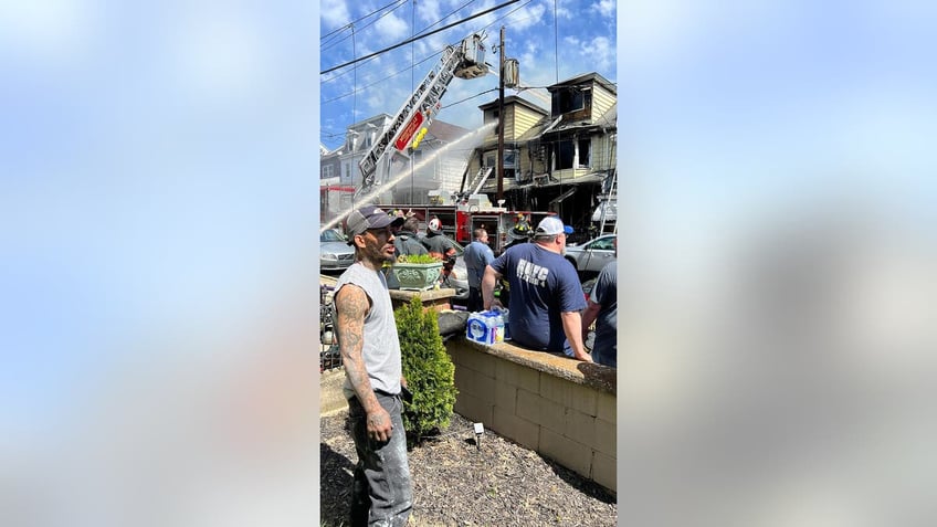 Fire rescue hero stands in the street as firefighters hose down the burnt-out house.