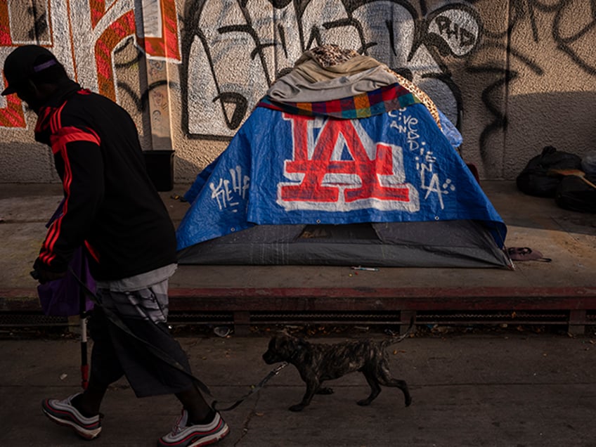 A man walks past a homeless encampment in downtown Los Angeles, Wednesday, Oct. 25, 2023.