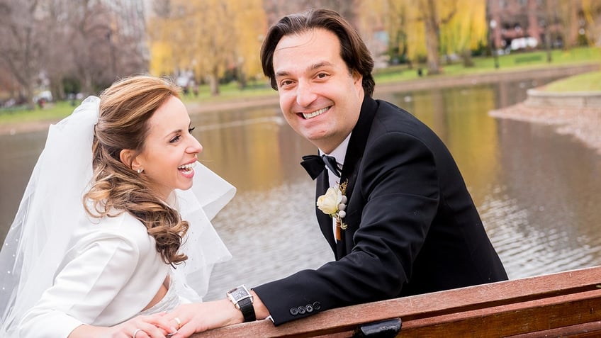 A bride and groom hold each other in a park in autumn.