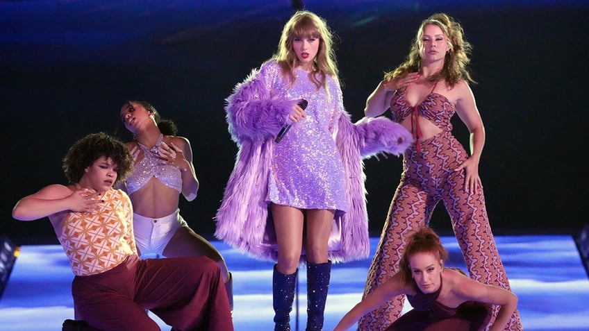 Taylor Swift struts down the catwalk in a purple dress and coat during her Eras Tour