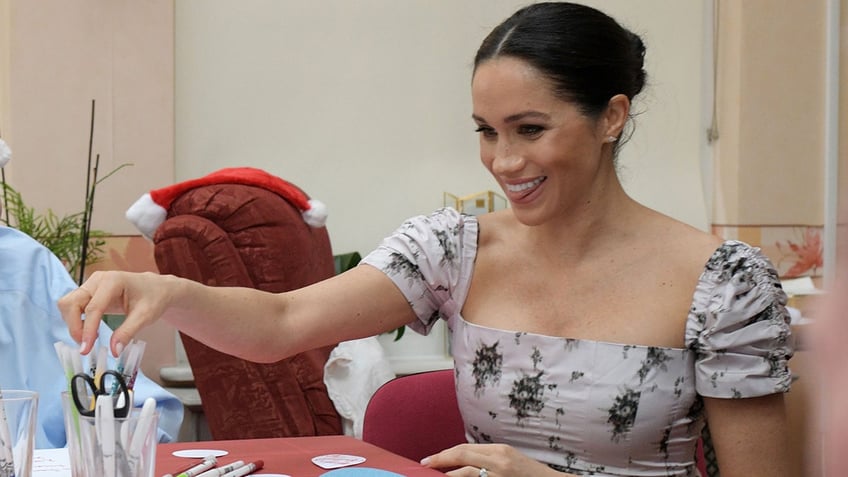 Meghan smiling as she goes to grab a pai of scissors