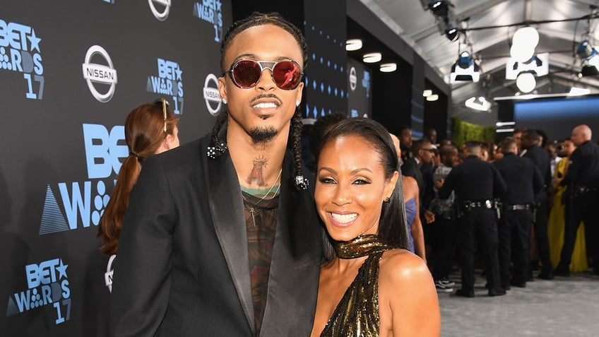 August Alsina and Jada Pinkett Smith smiling as they both wear black outfits