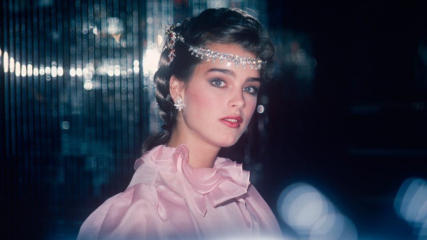 Brooke Shields in a pink ruffly dress with jewels draped over her head