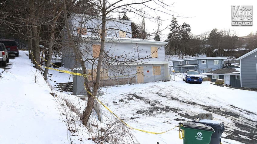 Windows to a two story house are boarded up with pieces of wood.