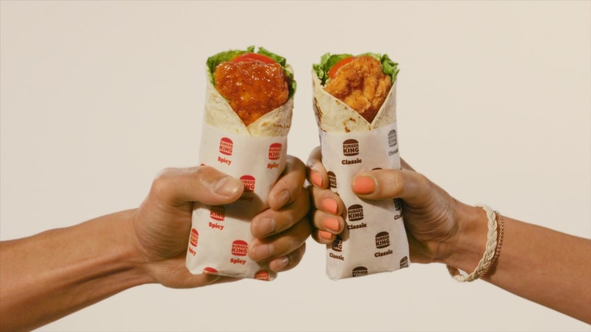 A man's hand holds a spicy Royal Crispy Wrap and a woman's hand holds a classic Royal Crispy Wrap from Burger King.